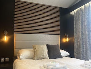 A hotel room with a bed, two wall-mounted light fixtures, and a textured curtain. - Romantic Coastal Chalet for 2 (Scherpenisse)
