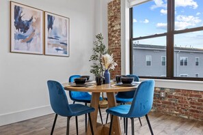 A dining area with a brick wall, a large window, and two abstract paintings. - 20 Min NYC Brick Loft w/ Gym, Desk & Parking (Kearny)
