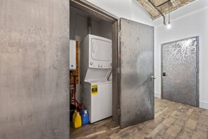 A laundry room with a washing machine, a door, and two detergent bottles. - 20 Min NYC Brick Loft w/ Gym, Desk & Parking (Kearny)