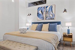A modern bedroom with a large bed, two bedside tables, a bench, and abstract wall art. - 20 Min NYC Brick Loft w/ Gym, Desk & Parking (Kearny)