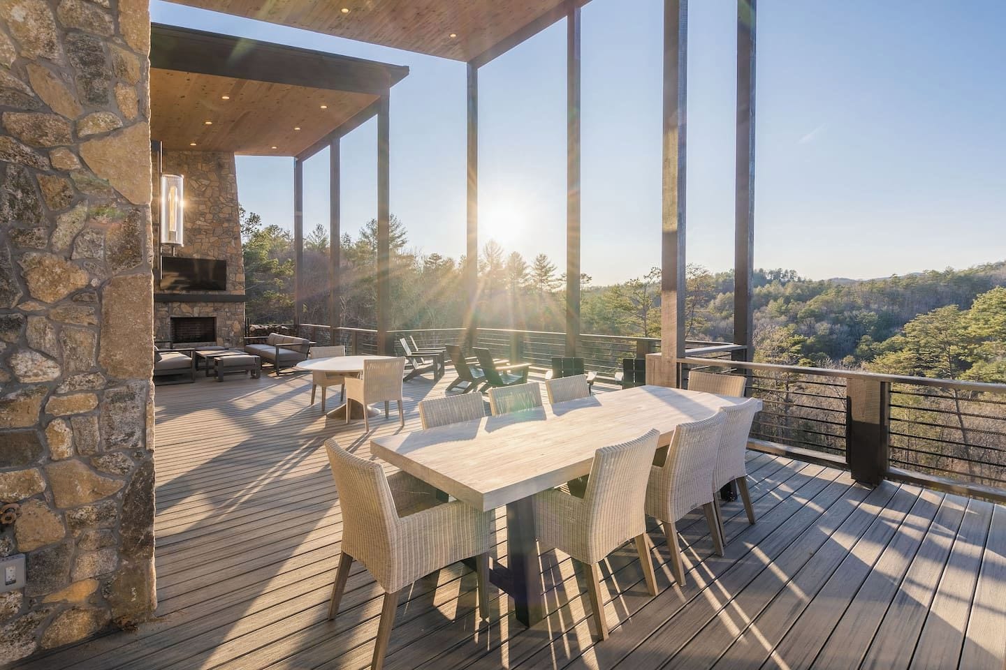 An outdoor deck with a stone wall, a table with chairs, and a view of a forested landscape.