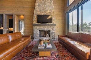 Una sala de estar con sofás de cuero, una chimenea de piedra, un televisor de pantalla plana y un ventanal grande.