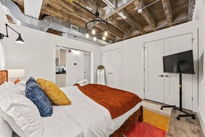 A modern hotel room with a bed, a television, and a kitchenette in the background. - Colorful Loft Gym, Patio + Parking Near NYC (Kearny)