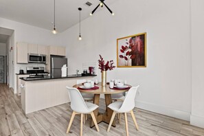 A modern kitchen with a dining area, featuring a central island, white chairs, and a table set for four. - Serene NJ Loft Sleeps 4 Gym + Free Parking (Kearny)