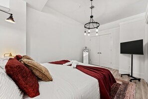 A modern bedroom with a large bed, a flat-screen TV, and a chandelier. - Serene NJ Loft Sleeps 4 Gym + Free Parking (Kearny)
