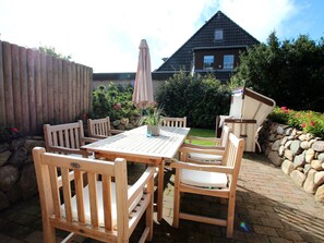 An outdoor patio with a wooden table and chairs, a potted plant, and a stone wall. - Holiday Home in Sylt With 3 Bedrooms (Sylt)