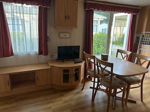 A room with a wooden cabinet, a television, a dining table with chairs, and a window with curtains.