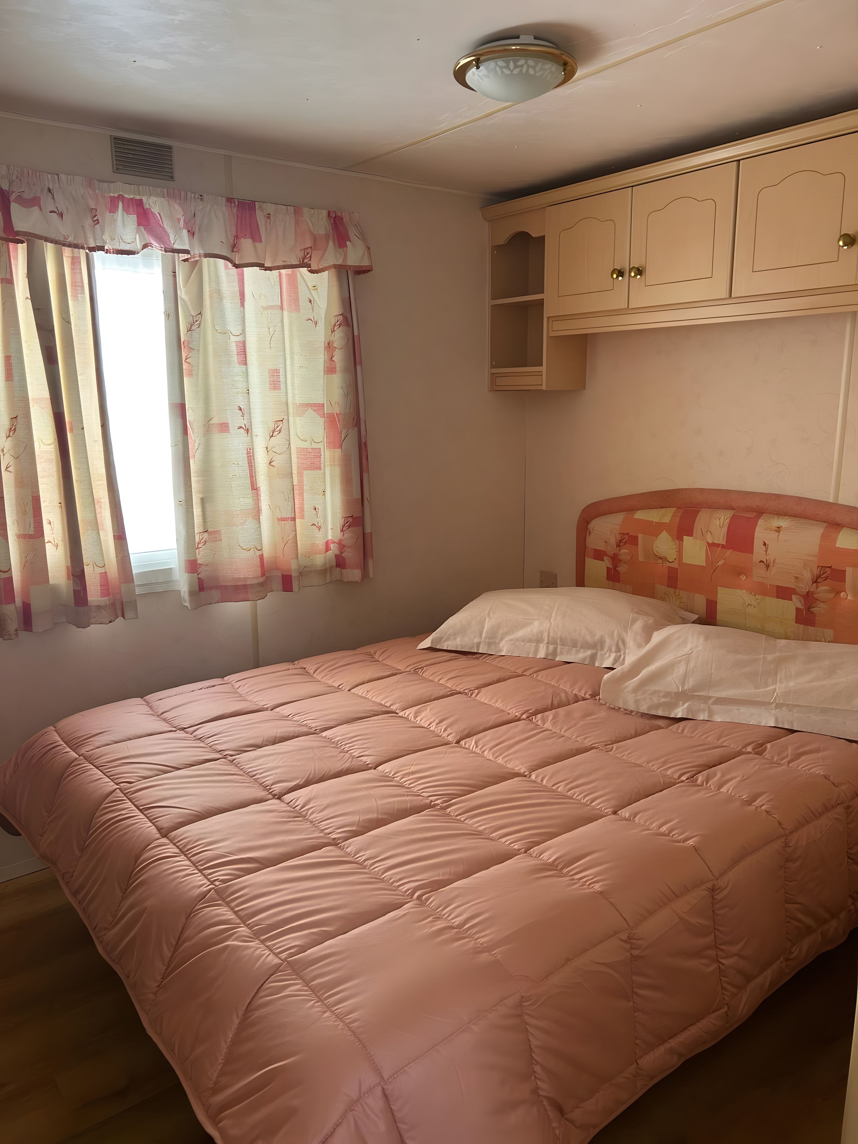 Ein Schlafzimmer mit einem Bett, einem Fenster mit Vorhängen, einer Deckenleuchte und einem Kleiderschrank.