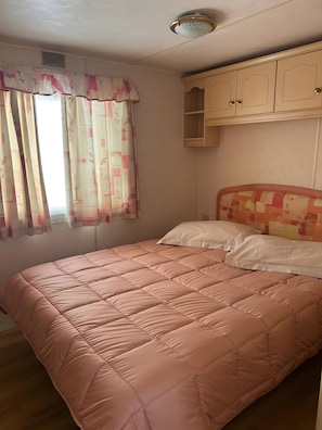 A bedroom with a bed, a window with curtains, a ceiling light, and a wardrobe.