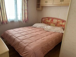A single bed with a pink quilt, a white pillow, and a headboard with a floral pattern.