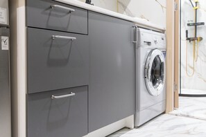 A modern laundry room with a gray cabinet, a washing machine, and a visible water hose. - StayShort - Spacious 11-Bedroom Villa Stay at Casa Royale, JVC (JVC)