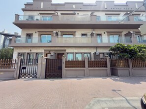 A multi-story residential building with a gated entrance, a balcony on the upper floor, and a paved driveway. - StayShort - Spacious 11-Bedroom Villa Stay at Casa Royale, JVC (JVC)