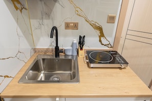 Een keuken met een roestvrijstalen spoelbak, een zwarte kraan, een inbouw inductiekookplaat en een marmeren achterwand.