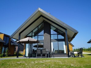 Ein modernes Gebäude mit großem Glasvordereingang, Außenbestuhlung und blauem Himmel.