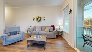 Una sala de estar con sofá, sillón y mesa de centro. Se ve una ventana con vista a un cuerpo de agua.