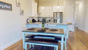 Una cocina moderna con armarios blancos, un refrigerador de acero inoxidable y una zona de comedor con una mesa y bancos azules.