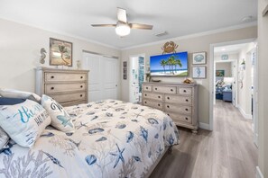 A bedroom with a bed, dresser, ceiling fan, and artwork on the walls. - Seashells Unit 43- Seahorse Ranch 2 Bedroom Condo (Sanibel)