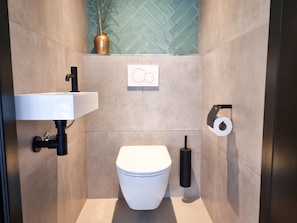 A modern bathroom with a white toilet, a wall-mounted sink, and a toilet paper holder. - Holiday Home in Aagtekerke With Wi-fi (Aagtekerke)
