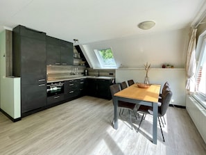 A modern kitchen with dark cabinetry, a wooden dining table, and a view of greenery through a skylight. - Holiday Home With 3 Bedrooms (Oostkapelle)
