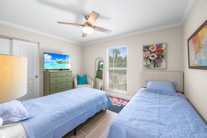 A bedroom with two beds, a ceiling fan, a TV, a dresser, and artwork on the walls. - Seashells Unit 31 2 Bedroom Condo (Sanibel)