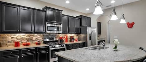 Cocina moderna con armarios oscuros, electrodomésticos de acero inoxidable, una isla de granito e iluminación colgante.