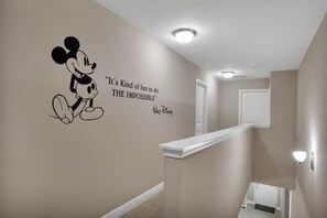 A hallway with a wall decal of Mickey Mouse and a quote, a white door, and a light fixture. - 7 Bed Private Pool/Spa & Themed Bedrooms 7 Home (Davenport)