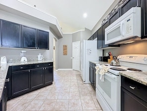 A kitchen with dark cabinets, a white refrigerator, a microwave, and a stove. - Luxury 5bd 3.5ba Pool Home In Windsor Palms Resort 5 Bedroom Villa (Kissimmee)
