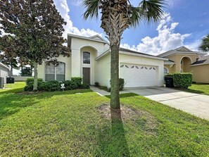 A residential house with a garage, a lawn, and a palm tree. - Luxury 5bd 3.5ba Pool Home In Windsor Palms Resort 5 Bedroom Villa (Kissimmee)