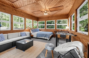 Interior acogedor de una cabaña con sofá, cama y mesa de fútbol de mesa, amplias ventanas que ofrecen vistas al follaje.