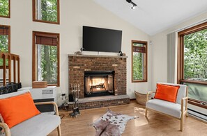 Un salon avec une cheminée, deux fauteuils, un téléviseur et de grandes fenêtres.