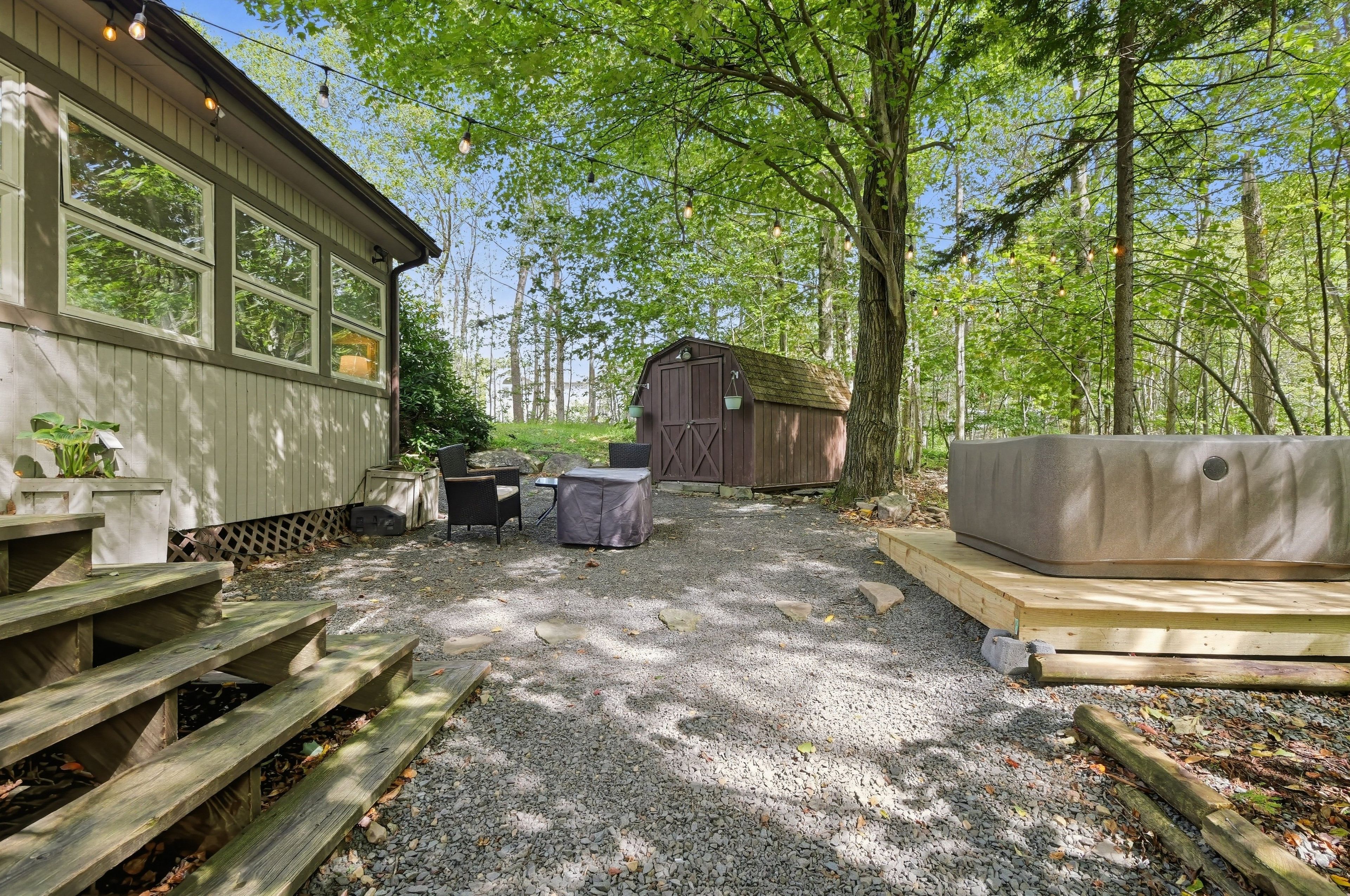 A rustic outdoor area with a wooden deck, a covered seating area, and a gravel path leading to a wooden structure.