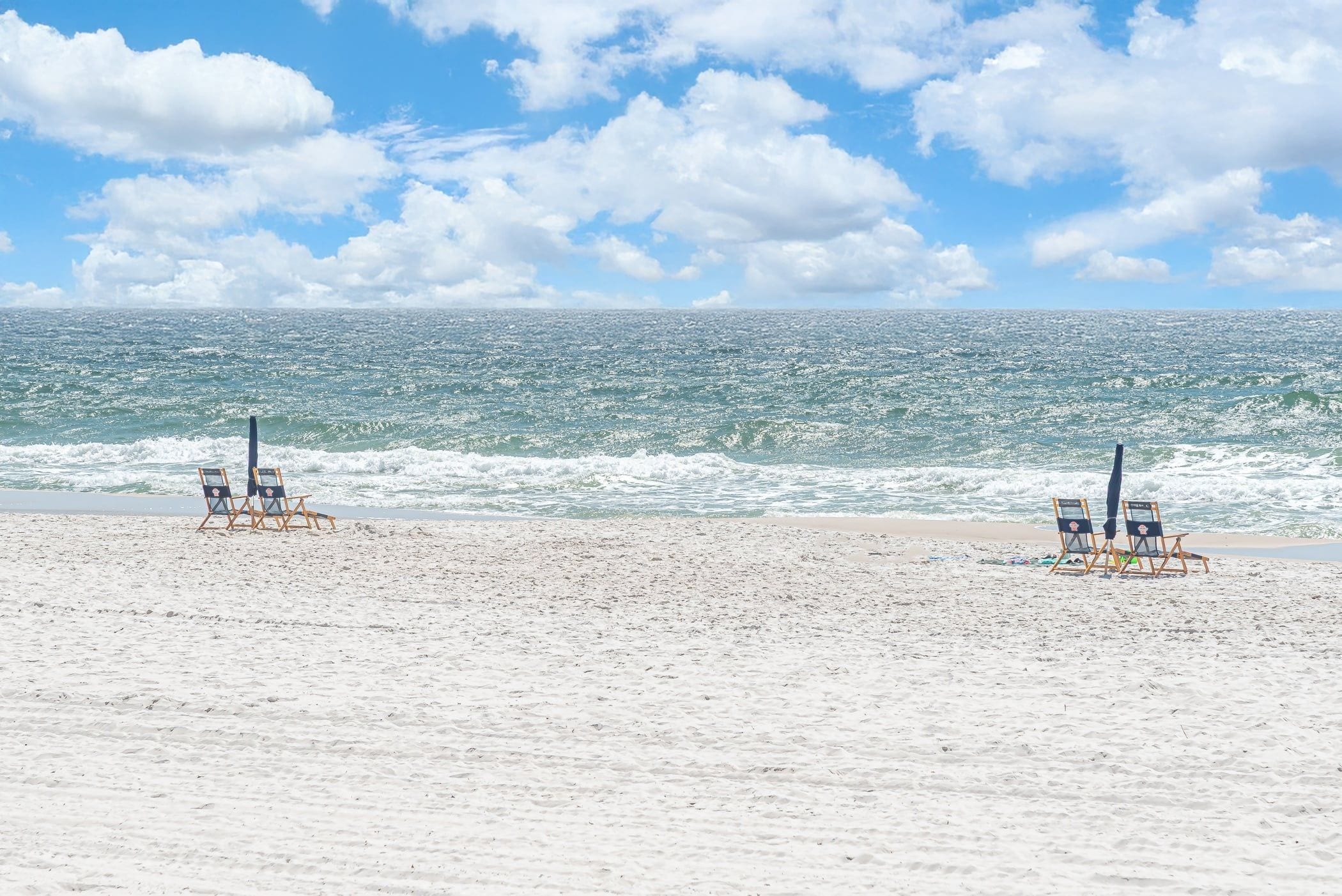 A beach with two wooden chairs and a signboard, sandy beach, and ocean waves.