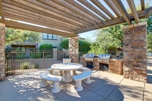 An outdoor patio with a round table and benches, a grill, and a stone pillar. - Villa Encore 3 Bedroom Townhouse (Scottsdale)