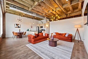 A spacious living area with a wooden ceiling, a dining table with chairs, and a kitchen in the background. - The Brickline Loft Near NYC + Gym + Parking (Kearny)