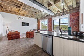 A modern kitchen with a large island, wooden beams, and a brick wall. - The Brickline Loft Near NYC + Gym + Parking (Kearny)