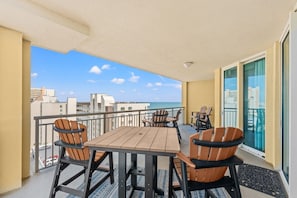 A balcony with a table and chairs, a view of the ocean, and a cityscape in the background. - Stylish ocean view condo with great amenities and spacious interiors | Mar Vista Grande - 1101 (North Myrtle Beach)