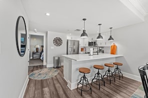 Cozinha moderna com ilha central, banquetas, iluminação pendente e um relógio na parede.