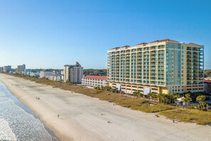 A beachfront hotel with multiple floors, a sandy beach in the foreground, and other buildings in the background. - Stylish ocean view condo with great amenities and spacious interiors | Mar Vista Grande - 1101 (North Myrtle Beach)