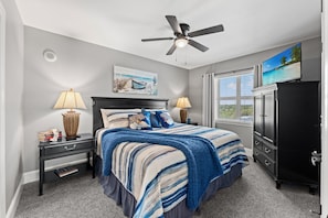 A bedroom with a bed, nightstands, a dresser, a ceiling fan, a window with blinds, and a painting on the wall. - Stylish ocean view condo with great amenities and spacious interiors | Mar Vista Grande - 1101 (North Myrtle Beach)