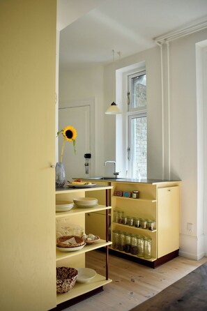 A kitchen with a window, a vase with a sunflower, and shelves with jars and dishes. - Newly renovated flat with balcony in Nørrebro (København)
