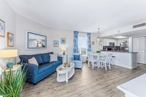 Un salon moderne avec un canapé bleu, une table basse et un coin repas avec des chaises blanches.