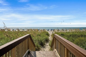 A wooden boardwalk leading to a beach with umbrellas and chairs. - Bay Watch Condo with floor to ceiling windows | Bay Watch Resort - 1641 (North Myrtle Beach)