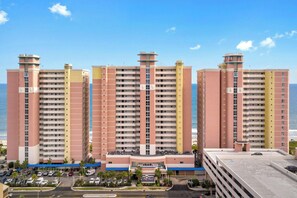A high-rise hotel with multiple floors, a central courtyard, and a view of the ocean. - Bay Watch Condo with floor to ceiling windows | Bay Watch Resort - 1641 (North Myrtle Beach)