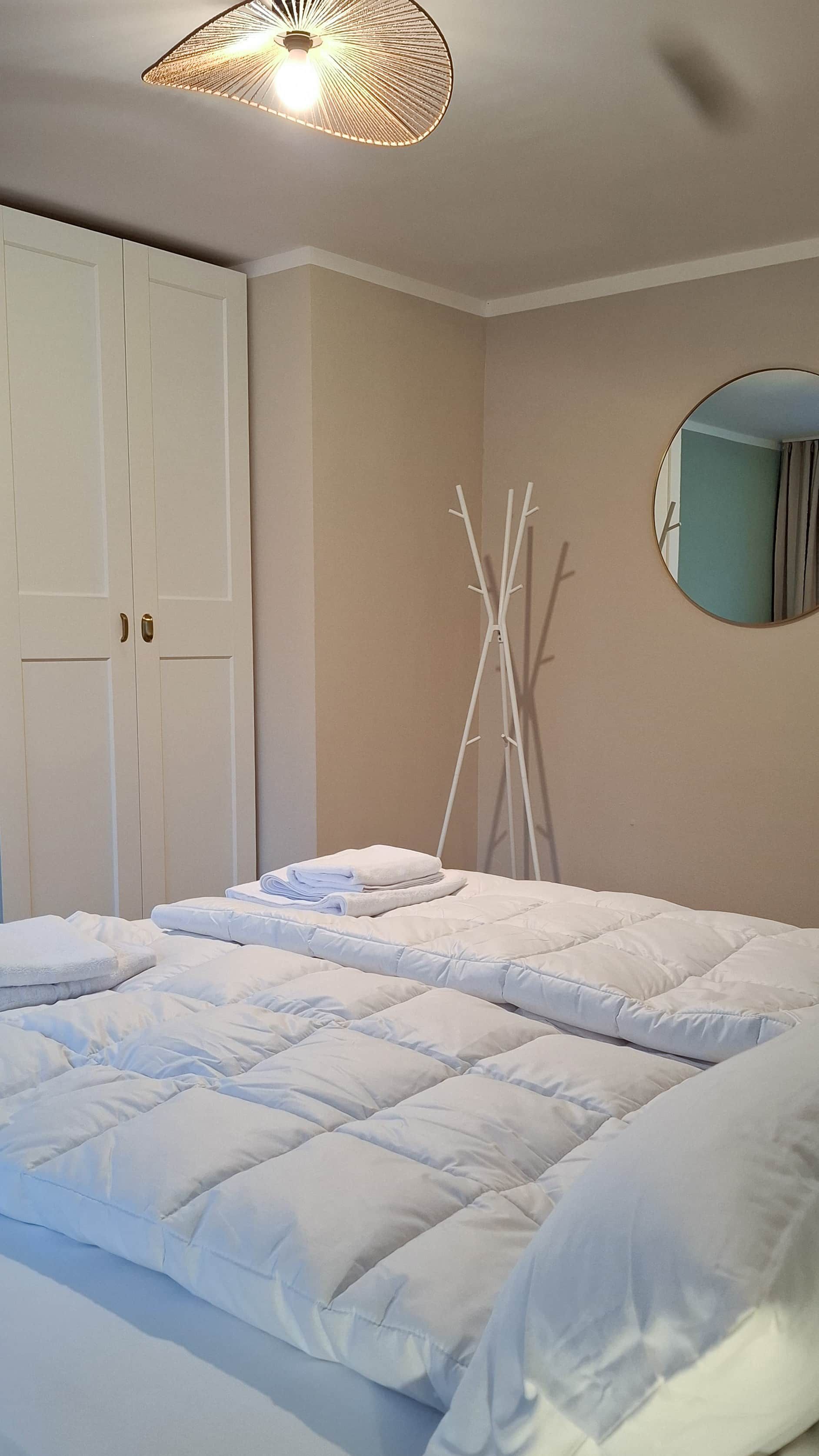 A bedroom with a bed, a wardrobe, a mirror, and a hanging light fixture.