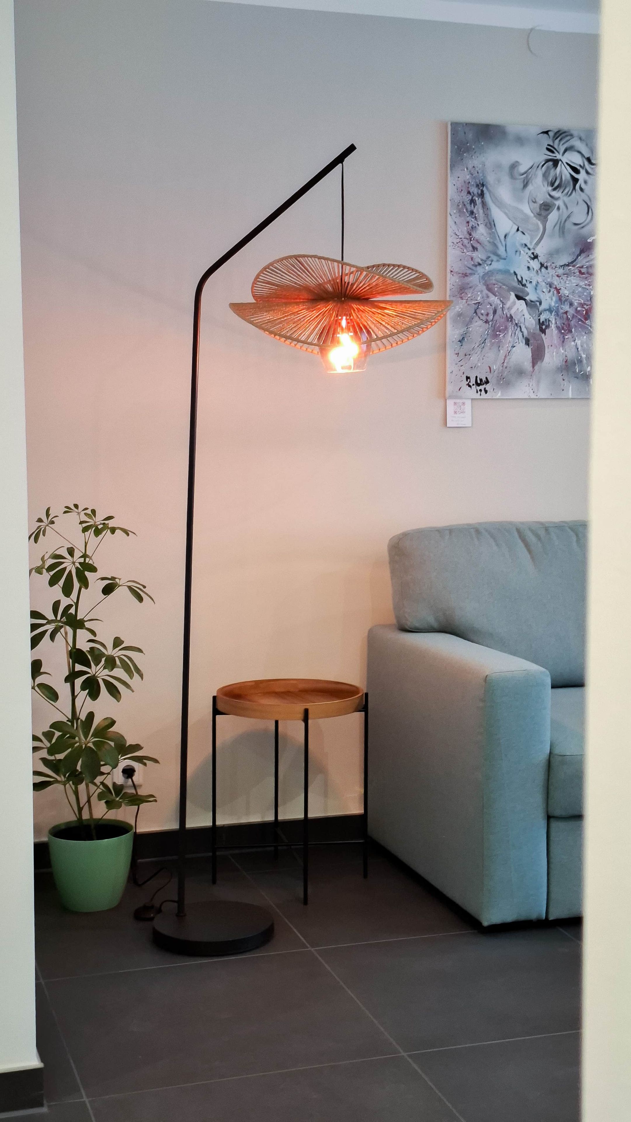 Ein modernes Wohnzimmer mit Stehlampe, rundem Holztisch, blauem Sofa und Kübelpflanze.