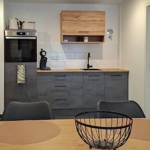 A modern kitchen with a built-in oven, a coffee machine, and a wooden cabinet above the countertop.