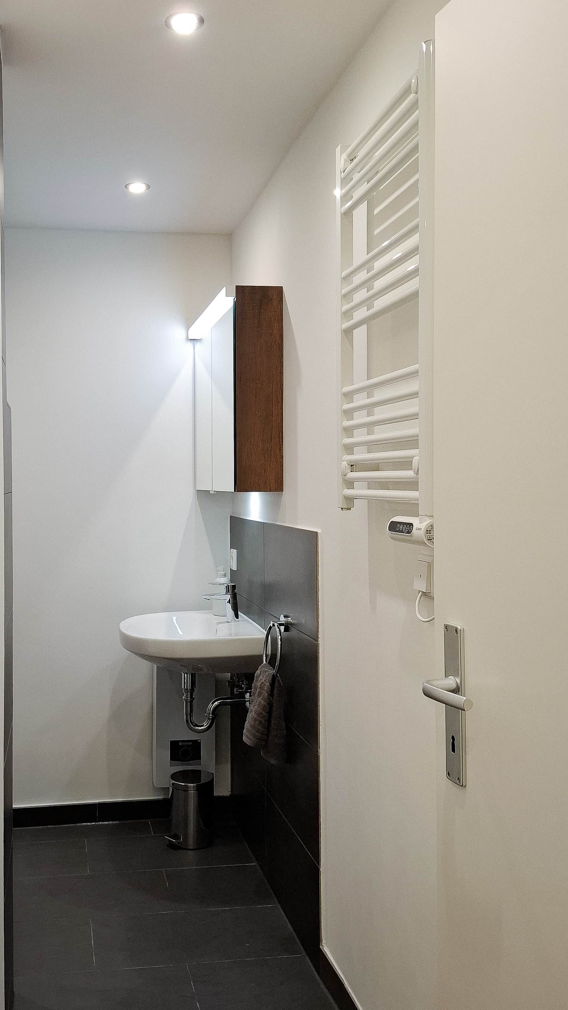 A modern bathroom with a white sink, a mirror, a towel rack, and a towel hanging on it.