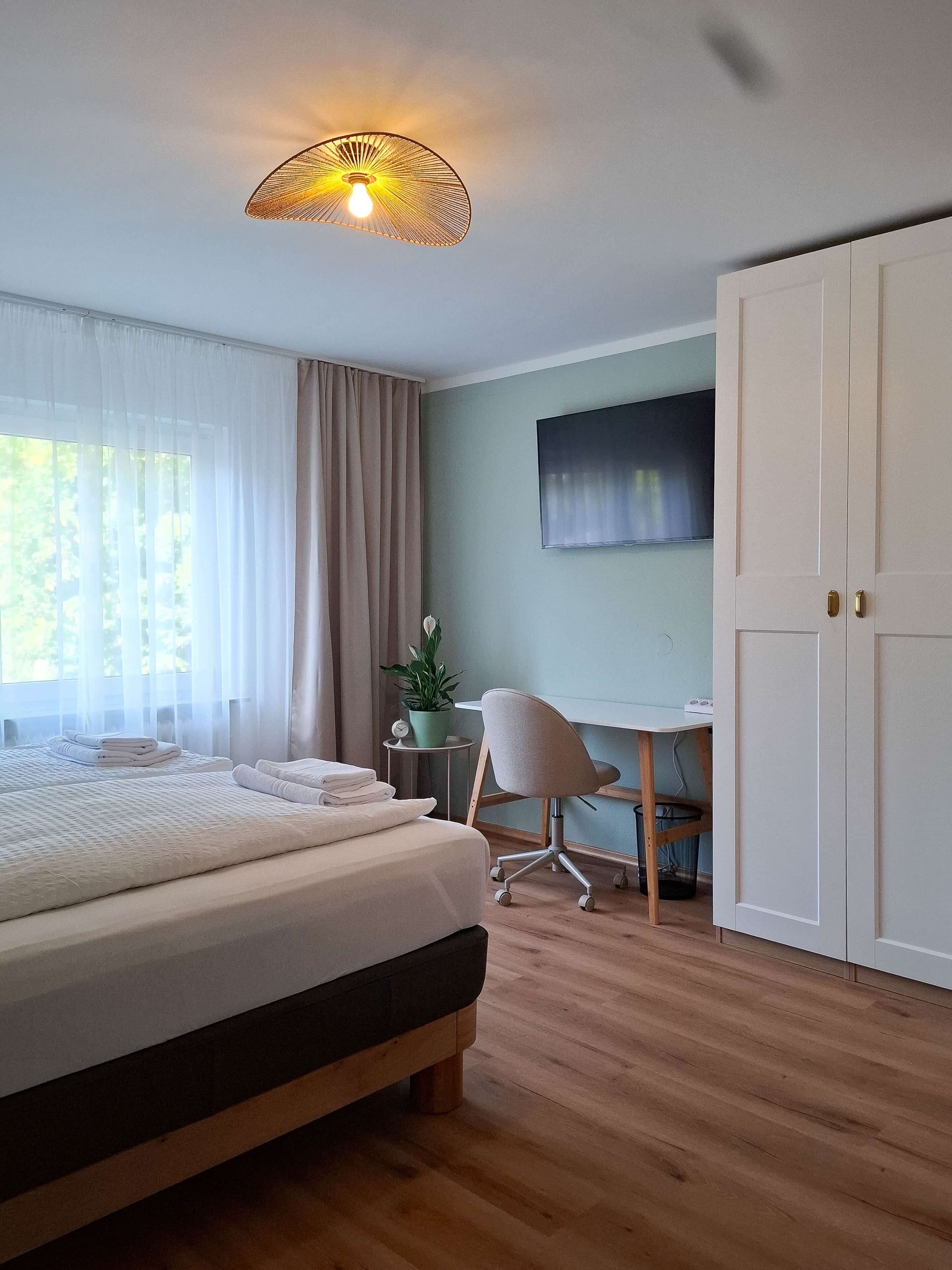 Ein Schlafzimmer mit einem Bett, einem Schreibtisch, einem Stuhl, einem Kleiderschrank und einer Deckenleuchte.