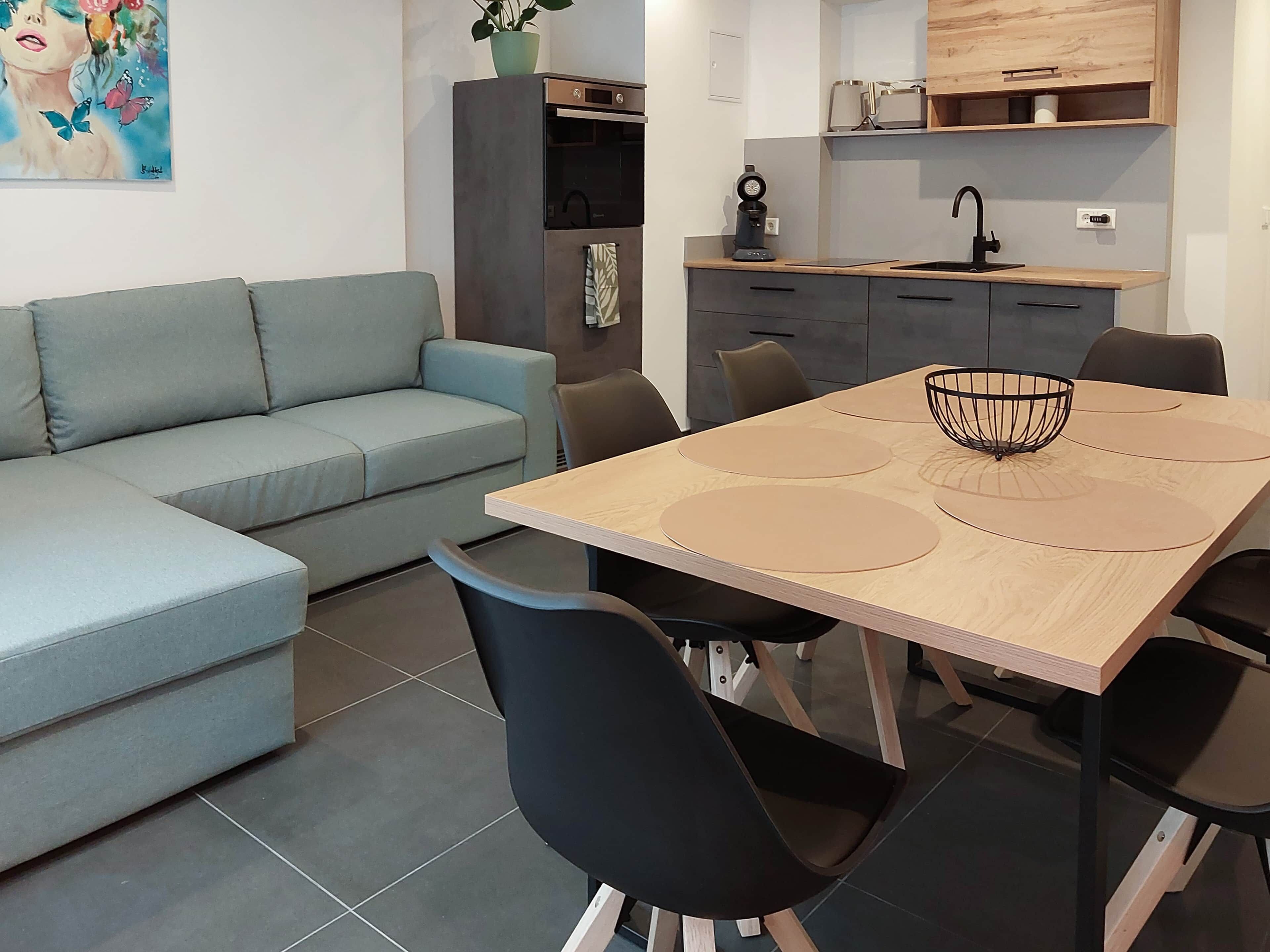 Ein modernes Wohnzimmer mit Sofa, Esstisch, Stühlen, einer Küchenzeile und einem Bild an der Wand.