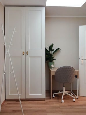 A room with a white wardrobe, a desk with a chair, a potted plant, and a floor lamp. - Nexpo Hub Apartment, 5 minutes from the trade show + parking (Nürnberg)